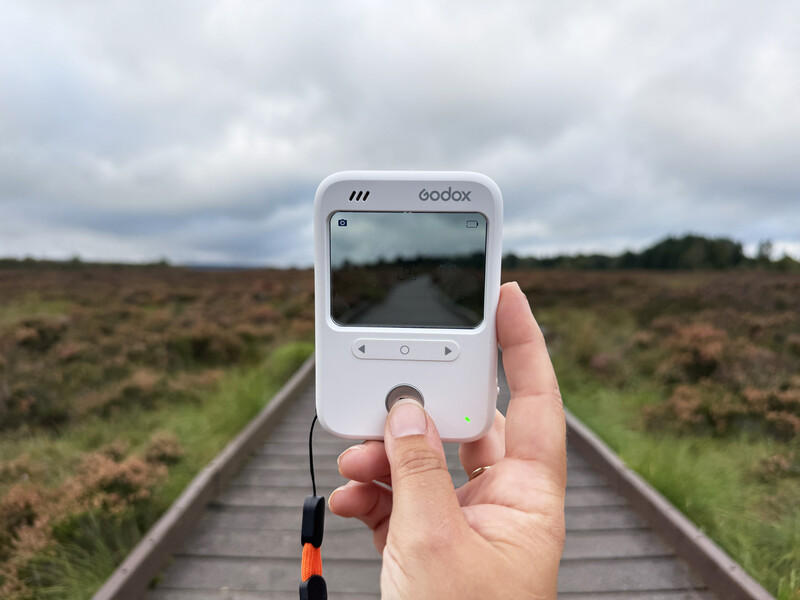 Hand holding a Godox light meter displaying a straight road through farmland