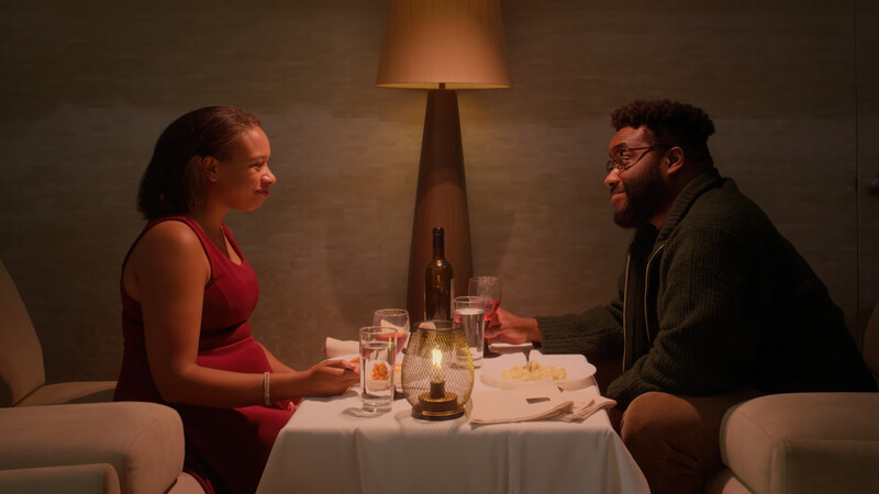 Two people seated at a formally set dinner table engaged in conversation
