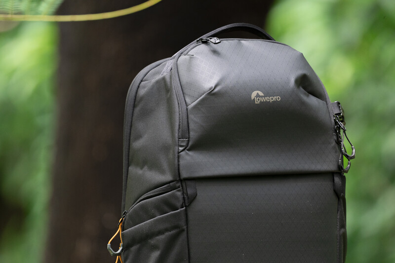 Lowepro black camera backpack with front compartment and carabiner clip against blurred green background