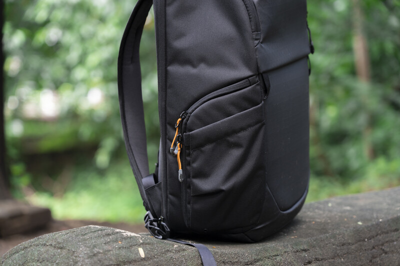 Black backpack with side pocket and orange zipper details resting on stone surface