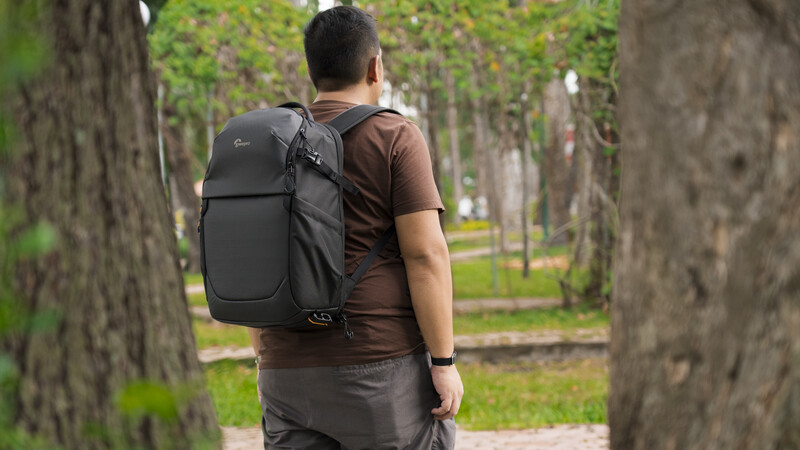 Man wearing dark backpack walking away through tree-lined park path
