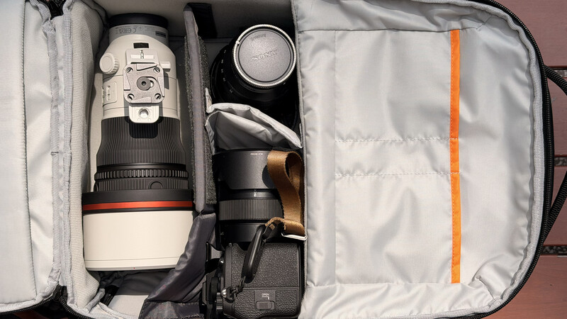 Camera gear organized in a padded travel bag with telephoto lens, camera body, and accessories