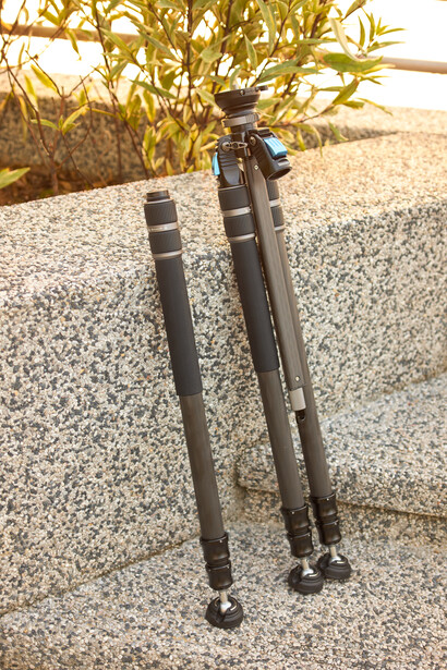 Two black camera tripod legs extended on gravel surface