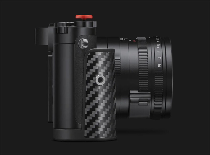 Black camera body in side profile with a textured carbon fiber hand grip, red shutter button, and a lens with visible aperture scale
