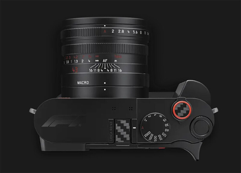 Overhead view of a black compact camera with a fixed lens and a red-accented shutter speed dial against a dark background