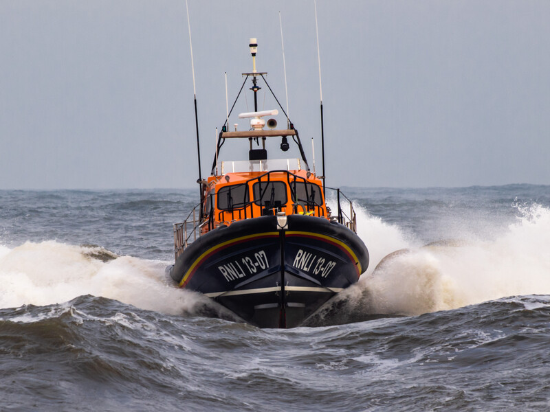 Orange and black lifeboat charging through large ocean waves in rough seas.