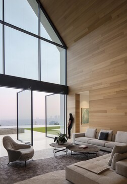Modern minimalist living room with floor-to-ceiling windows, wooden accent walls, and contemporary furniture overlooking a landscape.