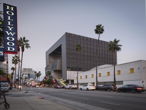Modern architectural building with dark grid facade next to white structure on Hollywood Boulevard with palm trees.