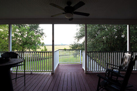 Interior view of a covered porch looking out toward a rural landscape through large windows and glass doors.