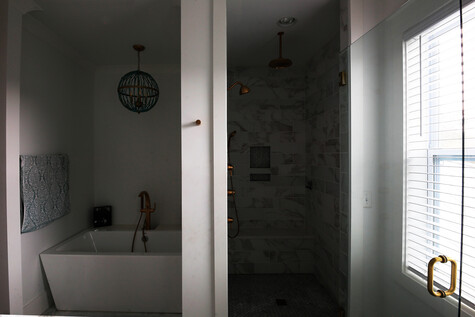 Modern bathroom with freestanding white tub, walk-in shower with dark tile, and natural light from window with shutters.