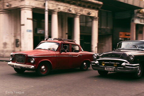 Two vintage automobiles parked on a city street with classical architecture in the background.