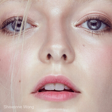 Close-up portrait of a woman's face with pale complexion, pink lips, and blue eyes looking directly at camera.