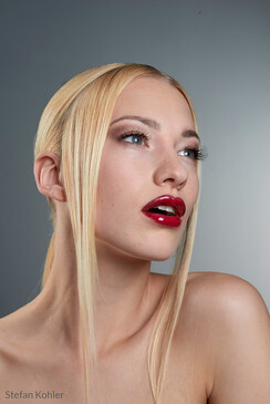 Woman with platinum blonde hair and red lipstick against neutral gray background.