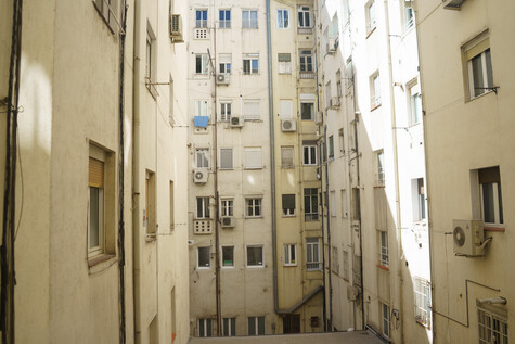 Narrow urban courtyard lined with cream and white residential buildings featuring multiple small windows and air conditioning units.