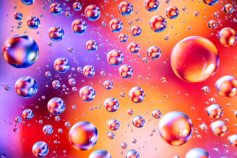 Colorful oil or soap bubbles floating against a vibrant gradient background transitioning from purple to orange and red.