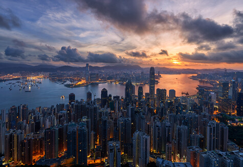 Dense urban skyline at dusk with illuminated buildings reflected in water below.
