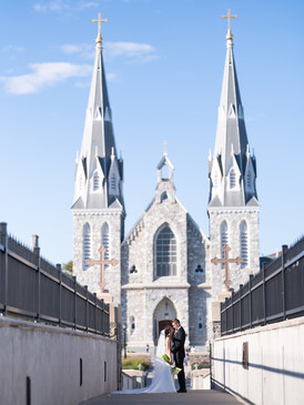 White neoclassical church with two tall spires and crosses, centered in frame with symmetrical approach.