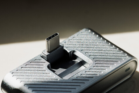 USB-C connector mounted on textured white device against neutral background with dramatic side lighting.