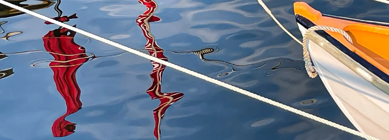 Moored boats with red rope reflections in still blue water, yellow and white hull visible on right.