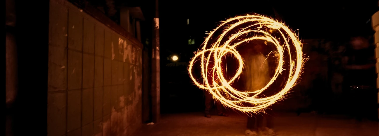 Long exposure of glowing fire trails looping into circles around a silhouetted performer on a dark night street