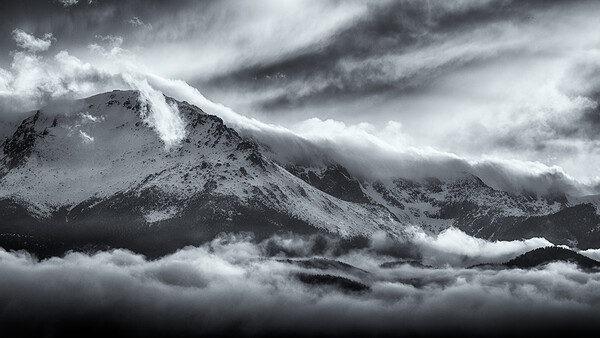 Snow-covered mountain peak shrouded in dramatic storm clouds and mist.