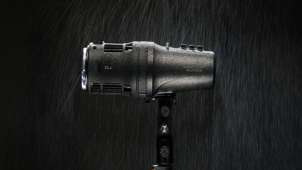 Studio flash unit mounted on a bracket, covered in water droplets against a dark background with rain streaks.
