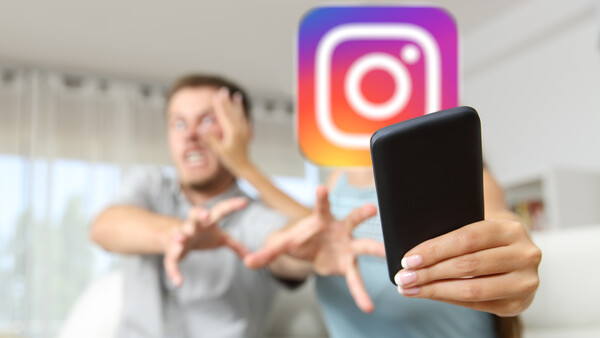 Man giving thumbs-down gesture with smartphone in foreground and Instagram logo in background.