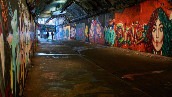 Underground tunnel lined with colorful graffiti murals under industrial lighting.