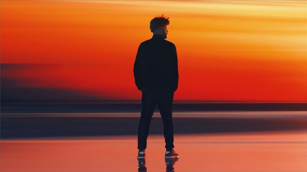 Silhouetted jogger standing on a reflective surface at sunset, facing the horizon.
