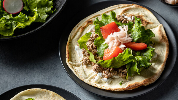 Plated taco with shredded meat, lettuce, tomato, and white crema on a dark round plate.