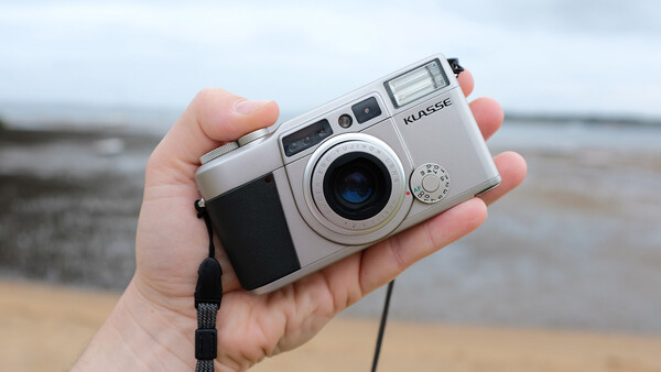 Silver rangefinder camera held in hand against a blurred coastal background.