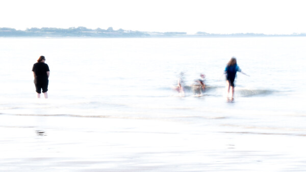 Multiple people wading in shallow ocean water with motion blur effect.