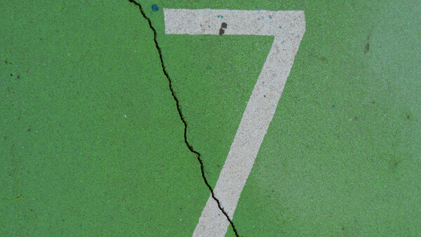 White painted number 7 on green asphalt with a diagonal crack running through it.