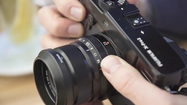 Hands holding a mirrorless camera with a prime lens attached, demonstrating proper grip and handling.
