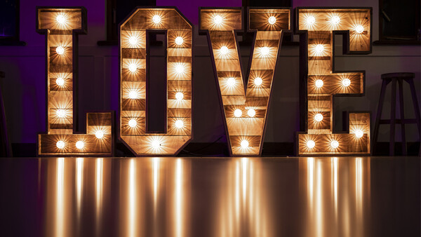 Illuminated marquee-style LOVE sign with warm bulbs against purple backdrop.