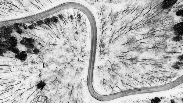 Aerial view of a winding road through snowy forest with dark evergreen trees creating strong contrast.