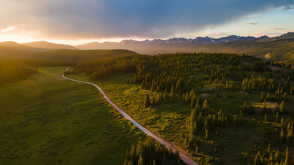 Aerial view of a winding river cutting through forested valley at golden hour with mountains in the distance.