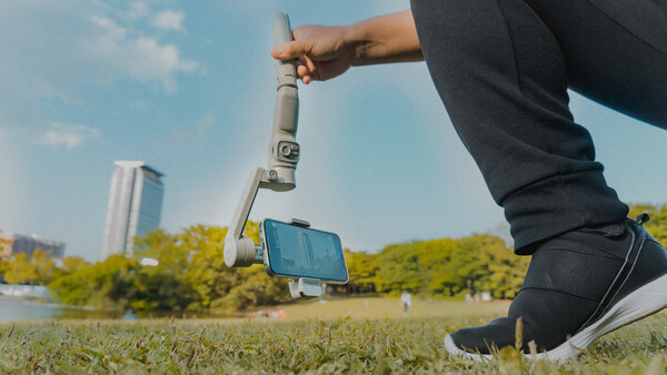 Person holding a surveying instrument and smartphone outdoors in a park setting.