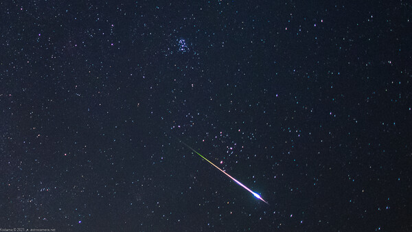 Bright meteor streaking diagonally across a starfield with a blue-white ionized tail.