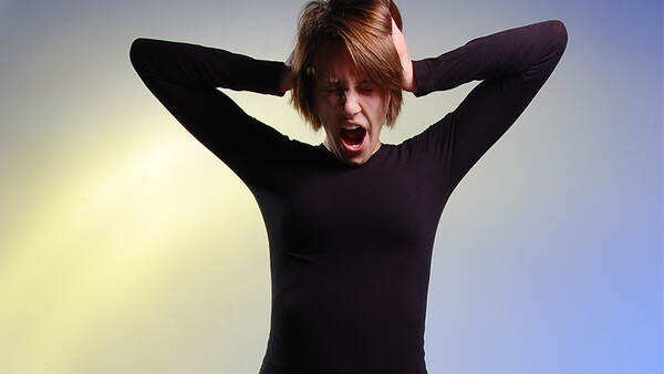 Person in black long-sleeve shirt with hands behind head, mouth open in an excited expression against a gradient blue and yellow background.