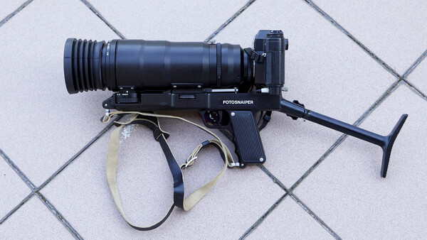 Fotograper film camera with telephoto lens mounted on light gray tile background.