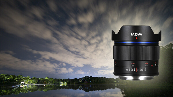 LAOWA ultra-wide angle lens with blue accent ring positioned against a nighttime landscape with reflective water and dramatic cloudy sky.