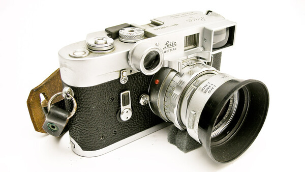 Vintage Leica rangefinder camera with interchangeable lens and brown leather strap.