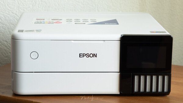 Epson EcoTank printer with white body and black ink tank cartridge module on wooden surface.