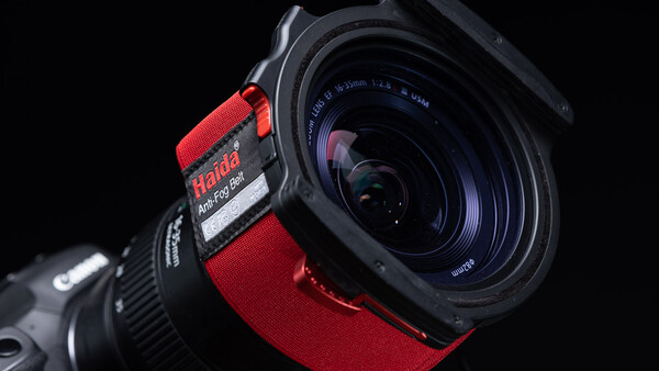 Wide-angle lens with red focus ring mounted on camera body against black background.