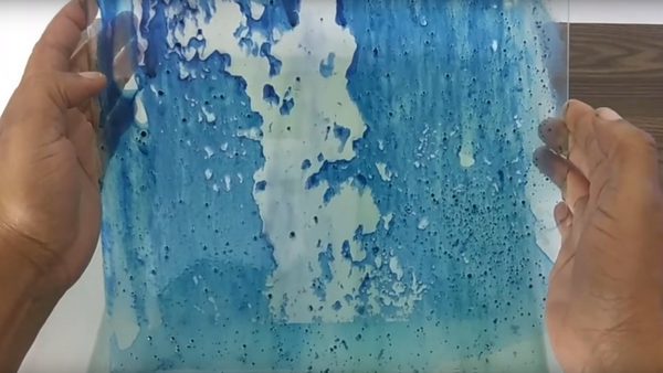 Hands holding a clear resin casting with blue and white swirled patterns and bubble textures.