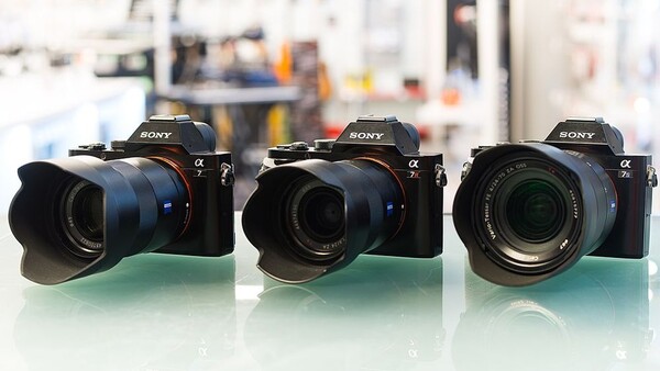 Three Sony Alpha mirrorless cameras with different lenses arranged side by side on a green surface.