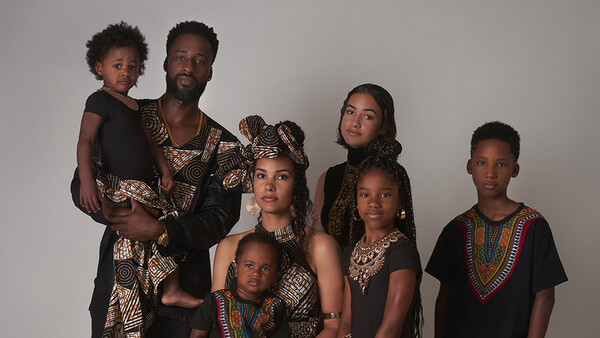 Family of seven posing together wearing coordinated black and patterned clothing against a neutral background.
