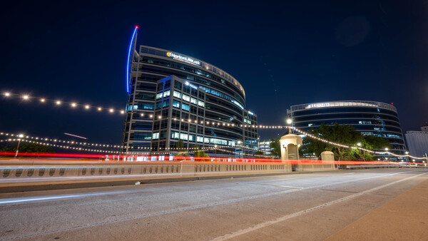 Modern curved office buildings illuminated at night with light trails from passing traffic on a bridge.