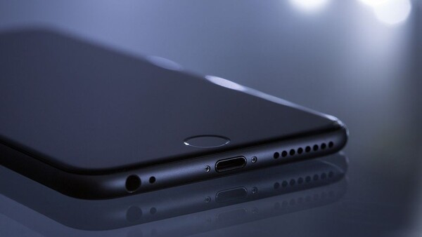 Dark smartphone positioned diagonally on reflective surface with side ports and speaker grille visible.